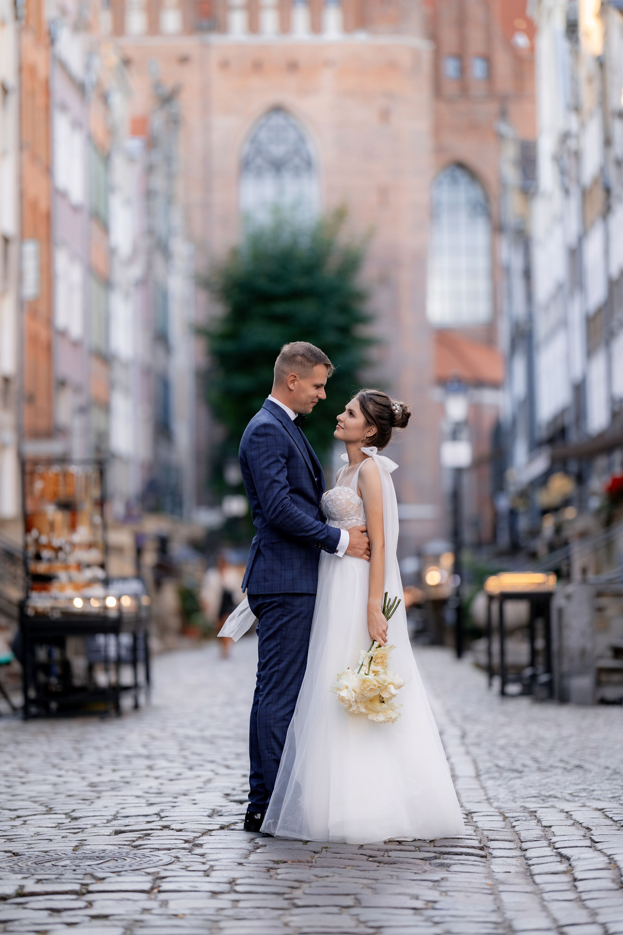 A romantic wedding portrait on cobblestone streets with historic architecture in the background.