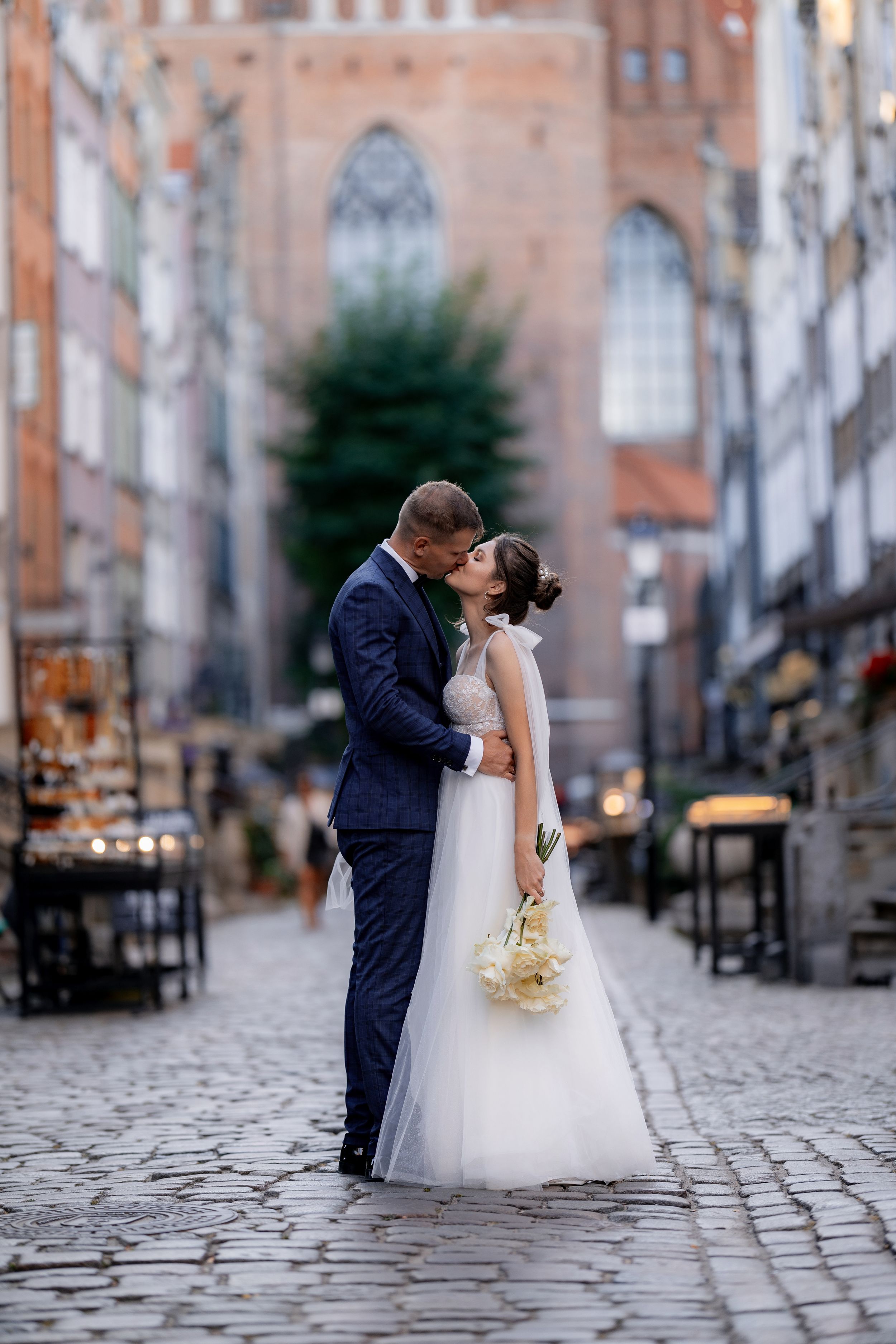 A romantic moment between newlyweds on a cobblestone street with gothic architecture behind them.