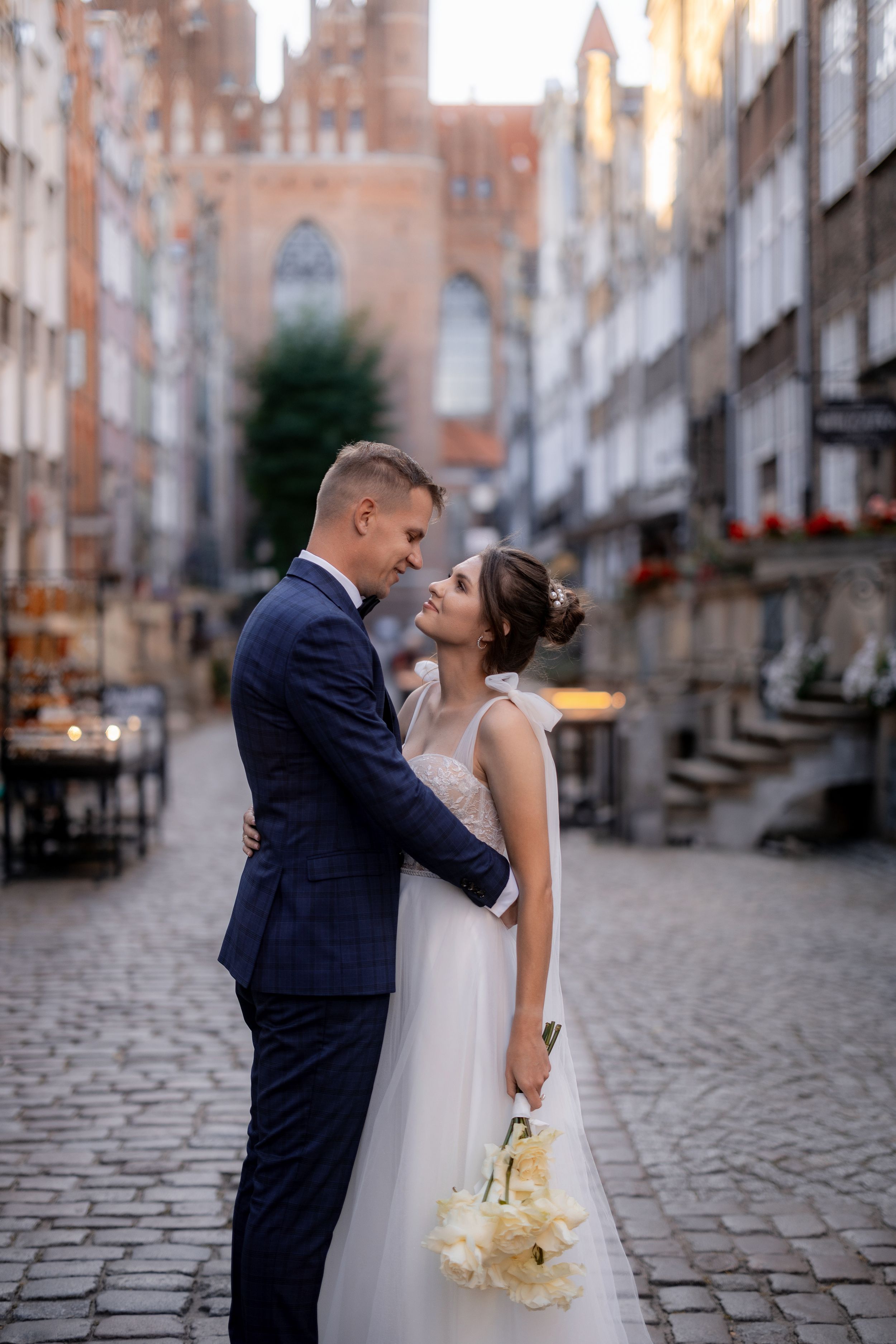 A romantic wedding portrait on a historic street with gothic church architecture in the background.