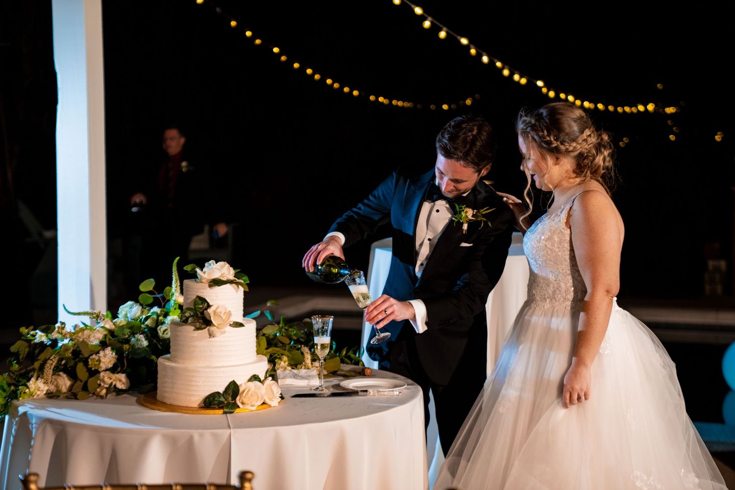 Wedding couple performs traditional cake cutting ceremony under string lights.