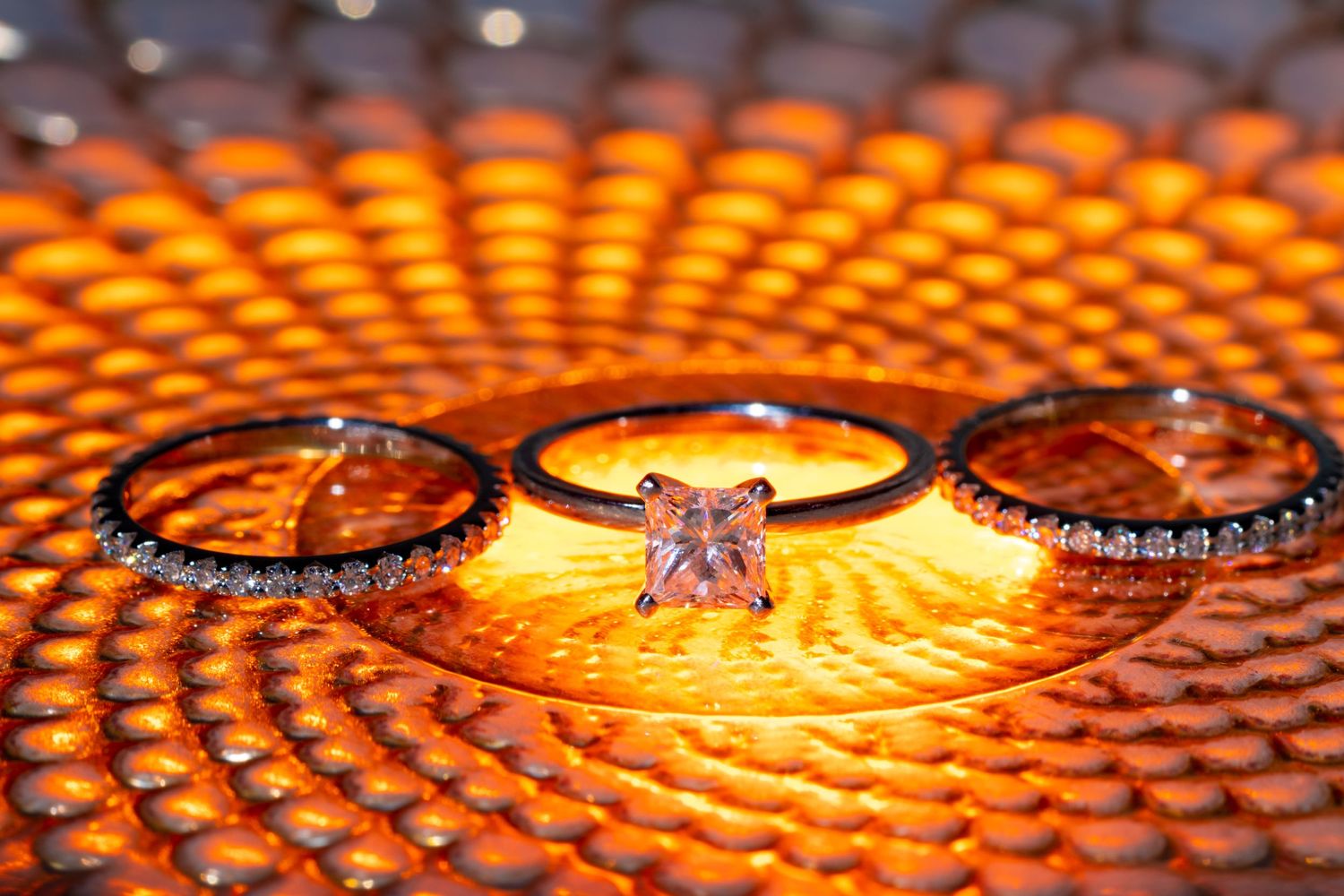 Three wedding rings beautifully displayed on a textured orange surface with dramatic lighting.
