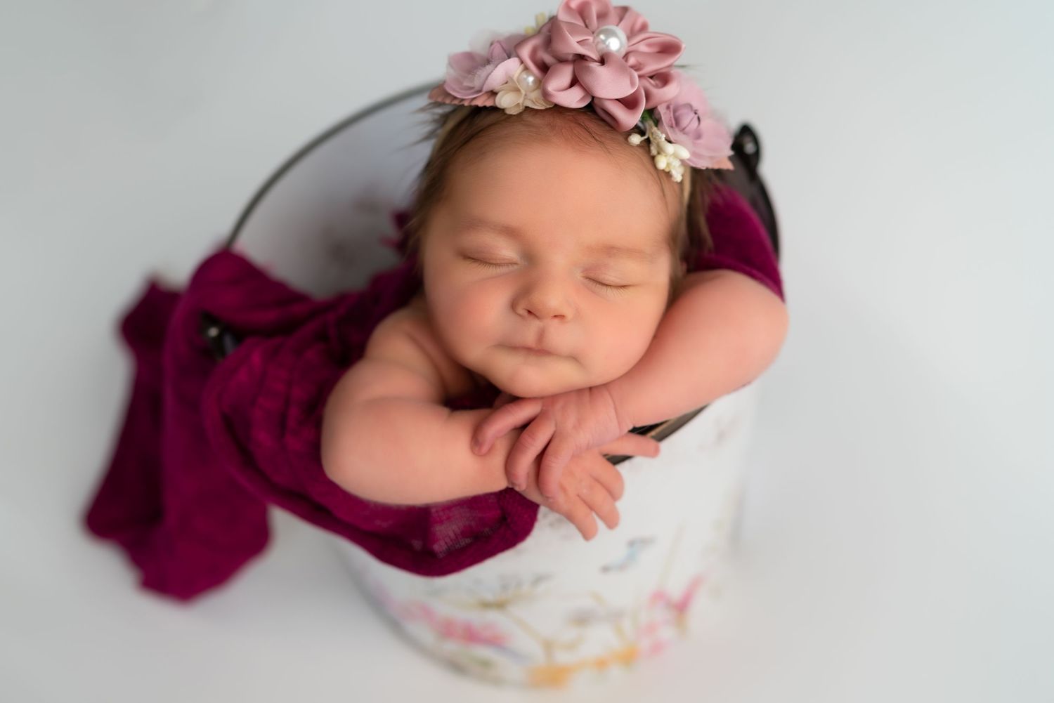 Sleeping newborn with pink floral accessories on white backdrop.