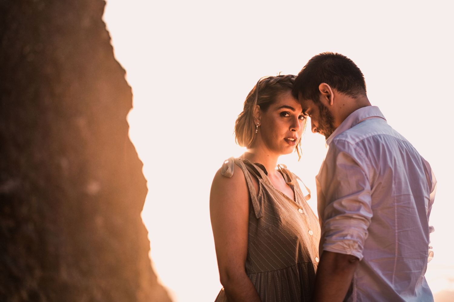 A romantic couple shares an intimate moment in warm sunlight against a rocky backdrop.