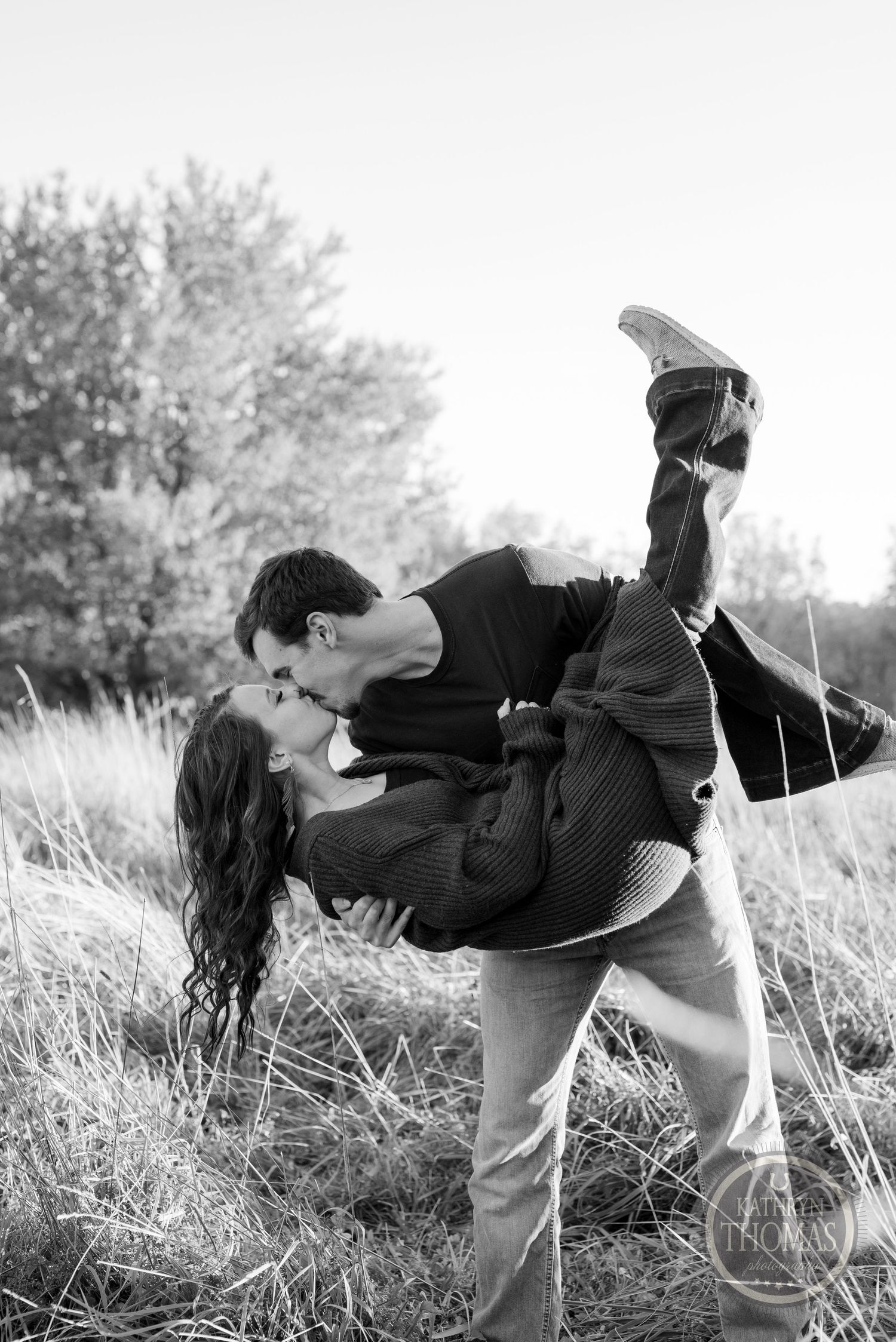 A romantic black and white photograph of a couple embracing in a field of tall grass.