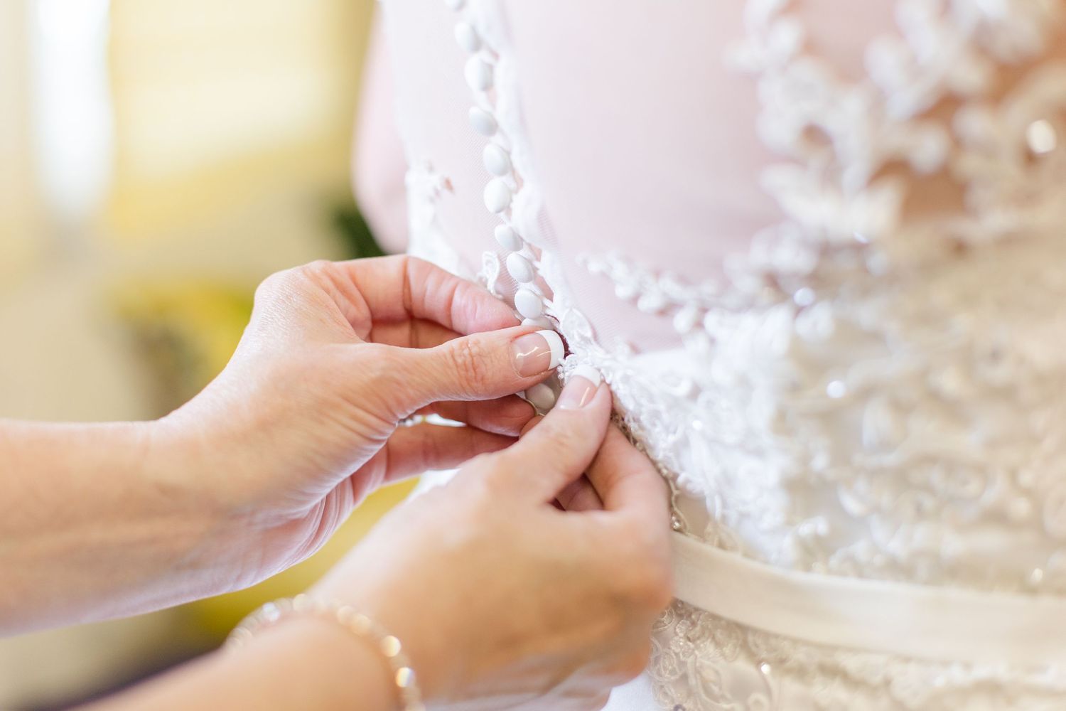 Close-up of hands adjusting delicate lace details on a wedding dress.