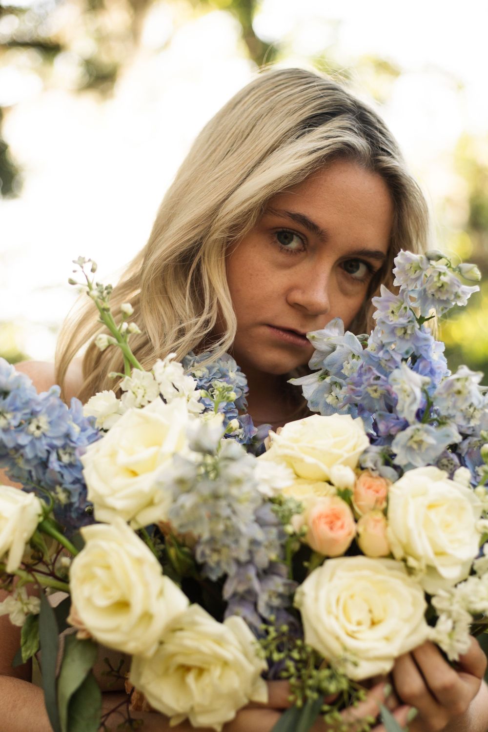 Moody portrait with a delicate bouquet of cream roses and blue delphinium flowers.