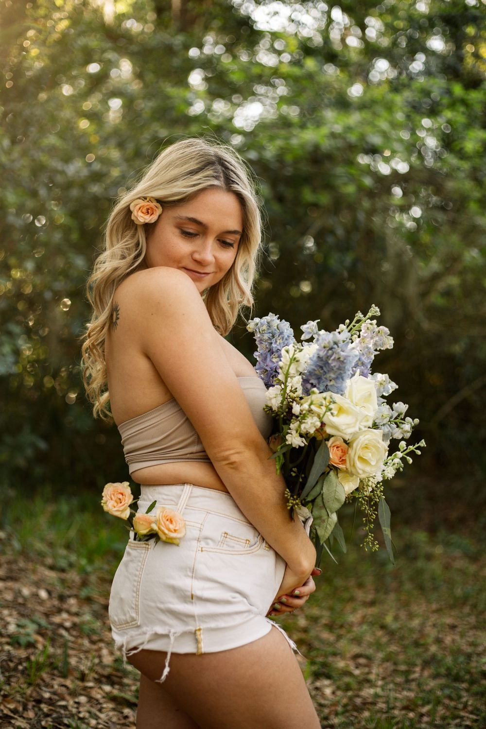 Artistic outdoor portrait with delicate flowers and a tan crop top against a sunlit natural backdrop.