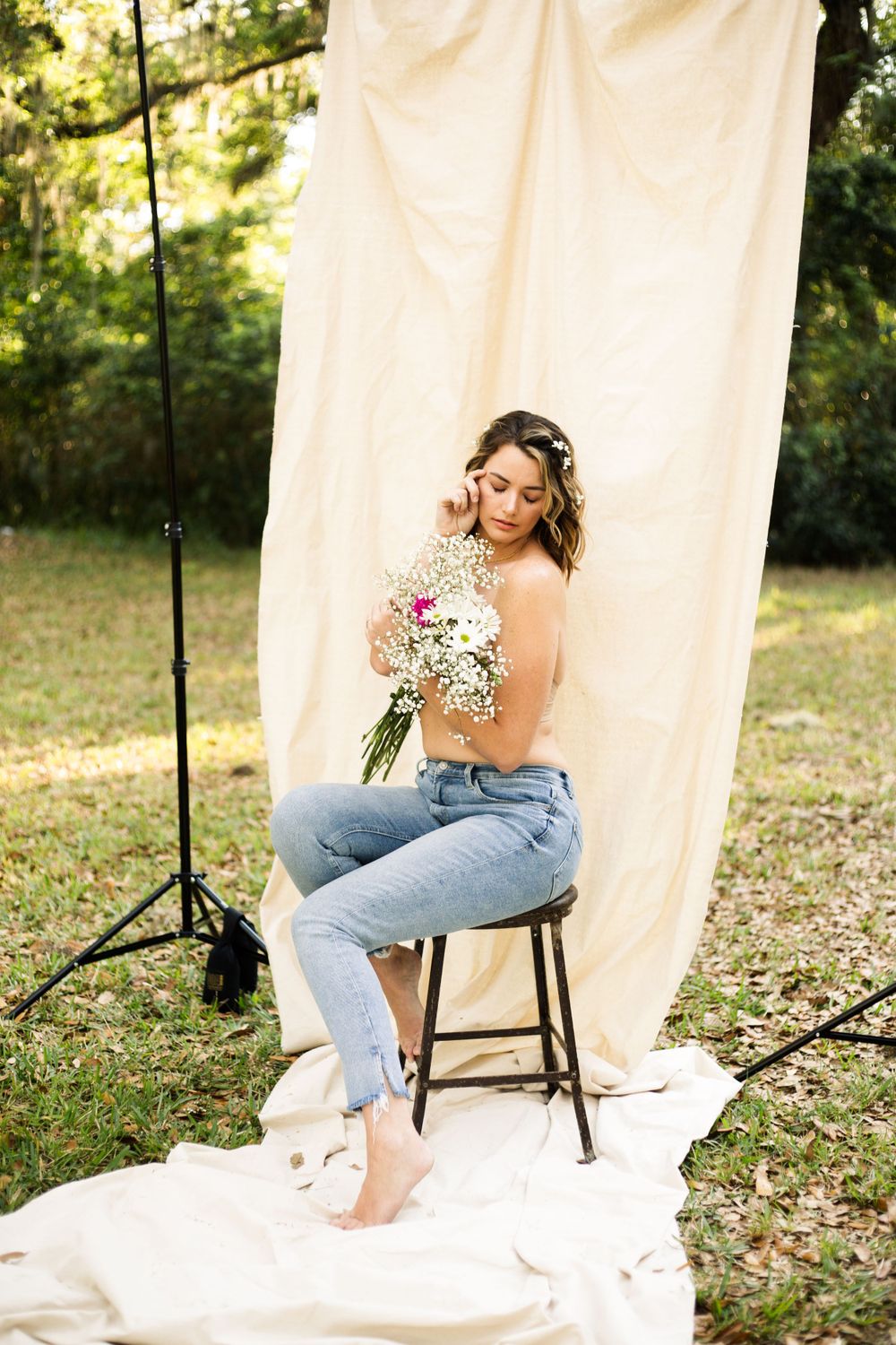 Natural light portrait on wooden stool with floral bouquet against cream backdrop.