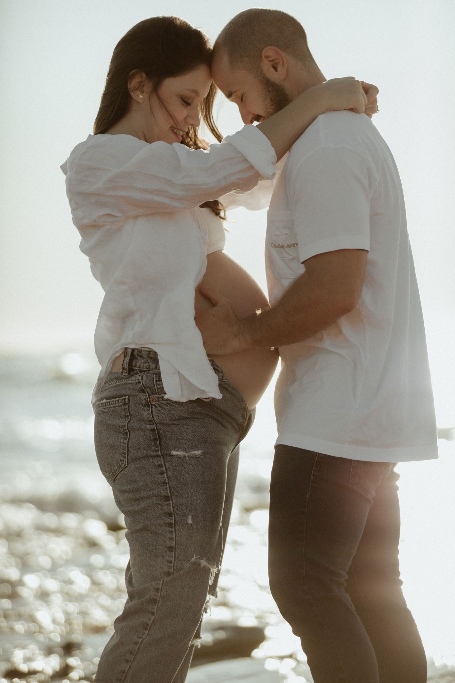Intimate couple embraces on beach during golden hour.