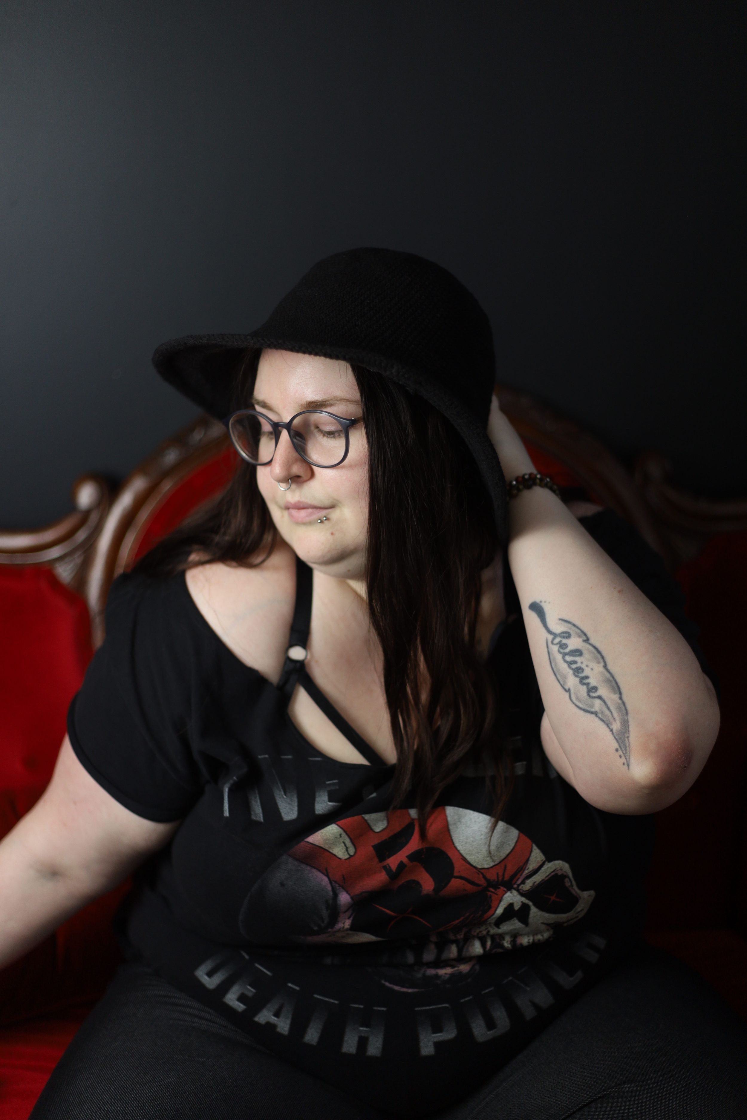 Alternative style portrait in black hat and band shirt against dark red backdrop.