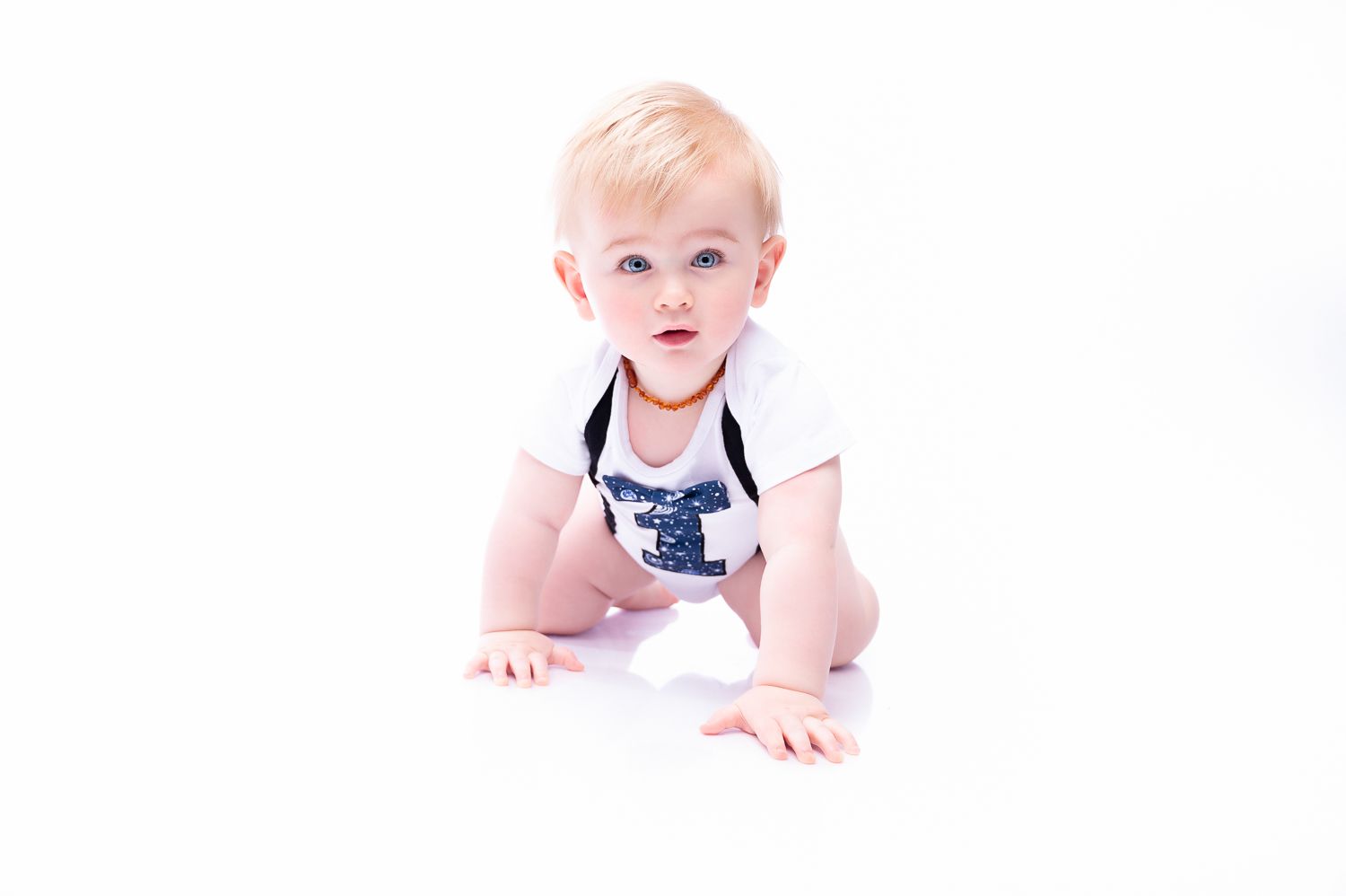 Baby in white outfit crawling on white background during studio photo session.