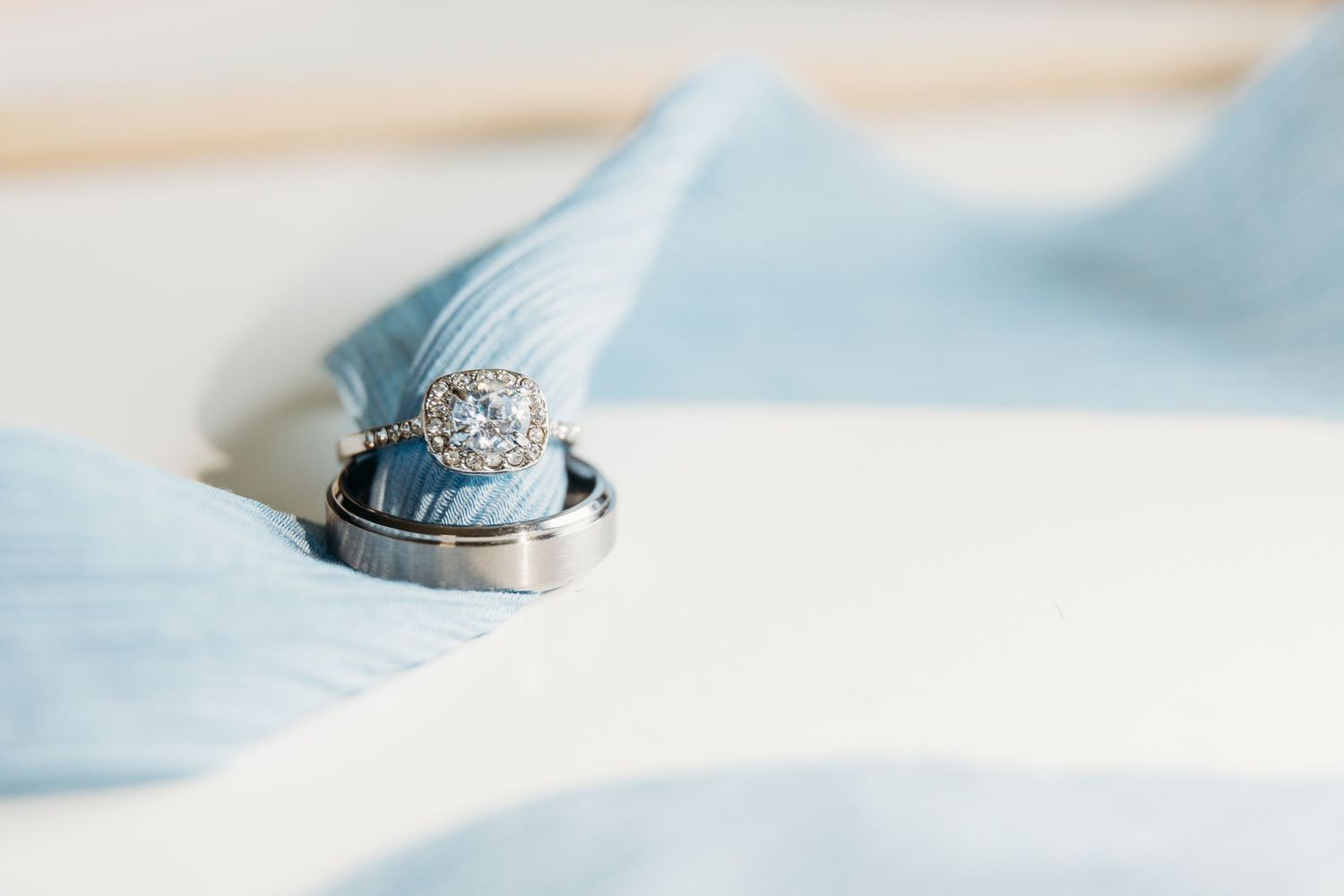Wedding rings rest on light blue fabric with a diamond engagement ring in focus.