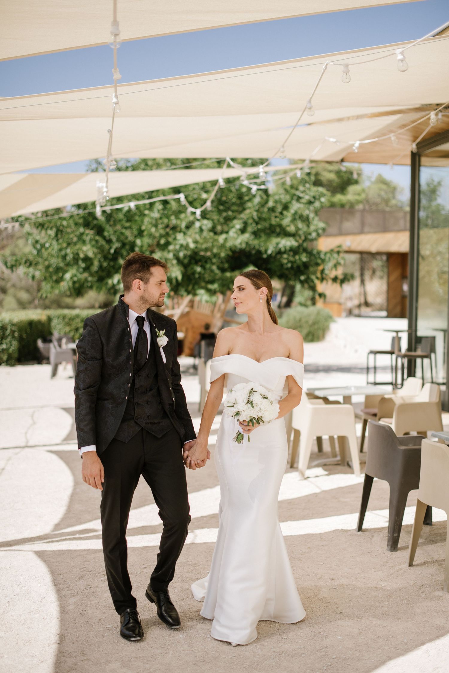 A couple walking together at an elegant outdoor wedding reception venue with white sun shades and modern decor.