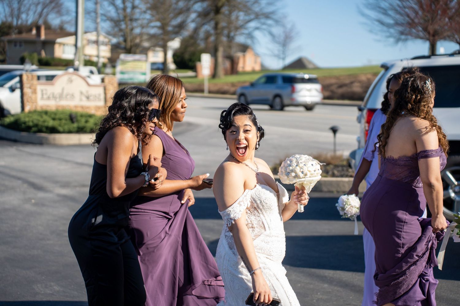 Wedding party members in purple dresses share a laughing moment outside.