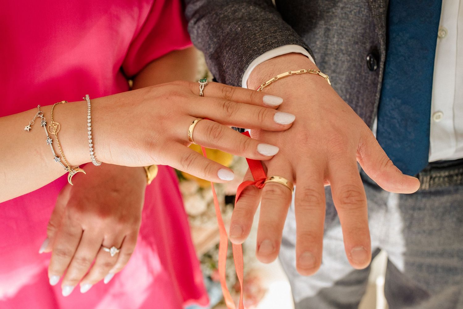 Close-up view of hands showing wedding rings and jewelry against pink and gray clothing.