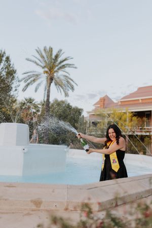 Graduate celebrates with champagne spray by resort pool during graduation photoshoot.