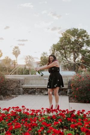 Graduate posing near vibrant red flowers during sunset photo session.