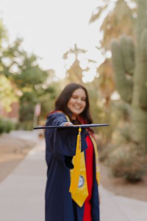 Graduate celebrating with cap and colorful stoles in a desert setting.
