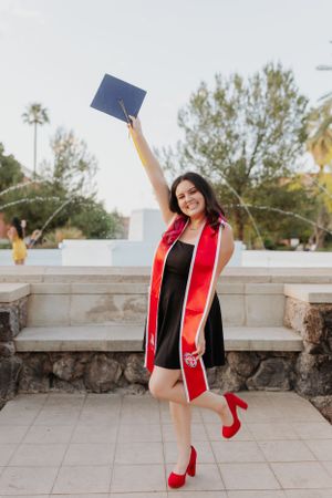 Graduate in academic regalia jumping joyfully during outdoor photo session.