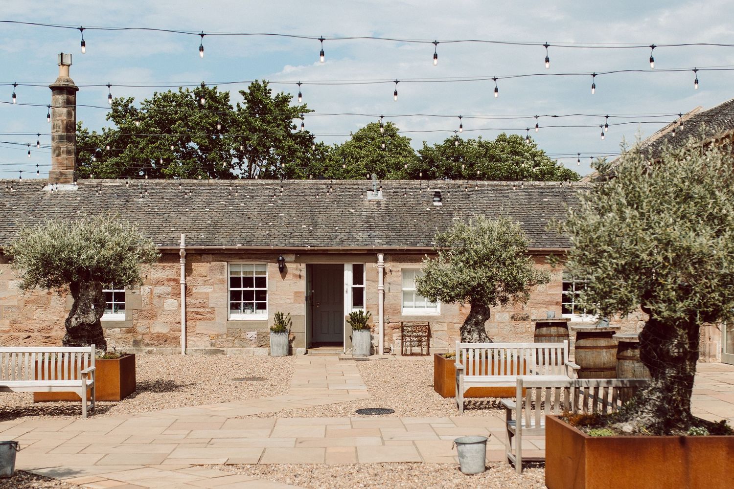 Rustic wedding venue with string lights and stone buildings under blue skies.