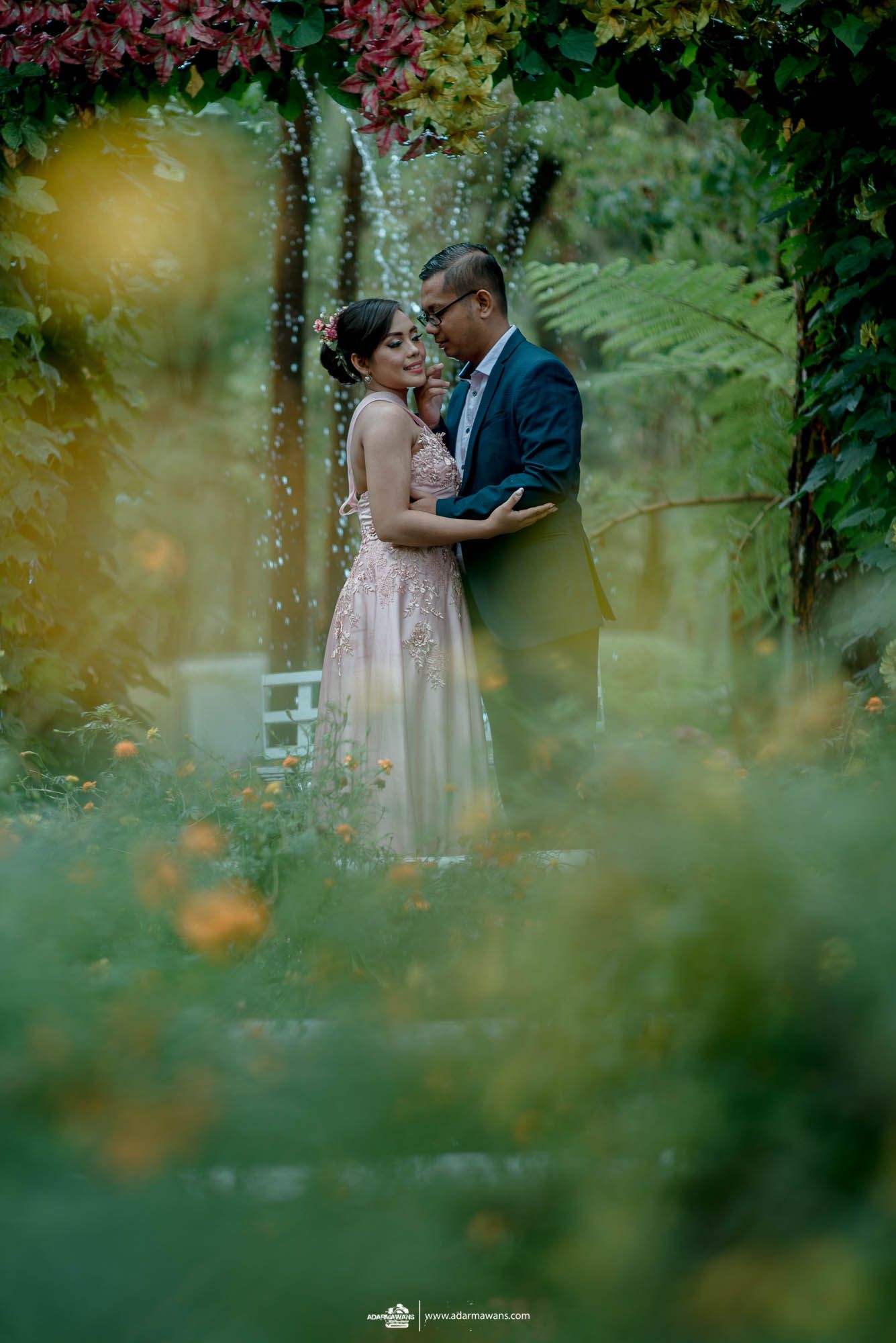 Romantic garden portrait with couple embracing among lush foliage.