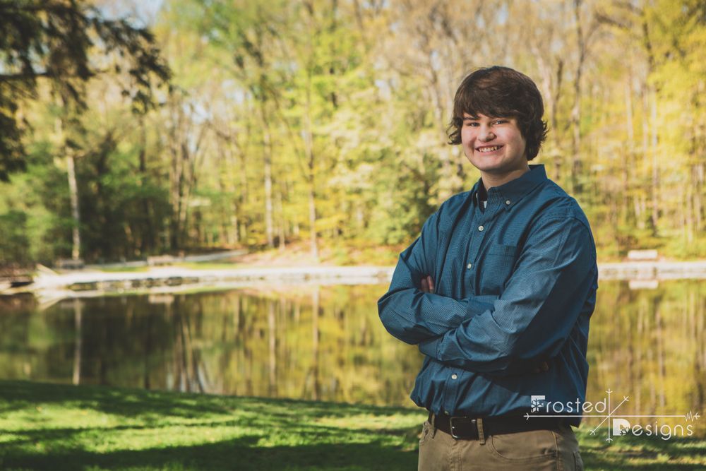 High school senior boy in front of lake in the woods.