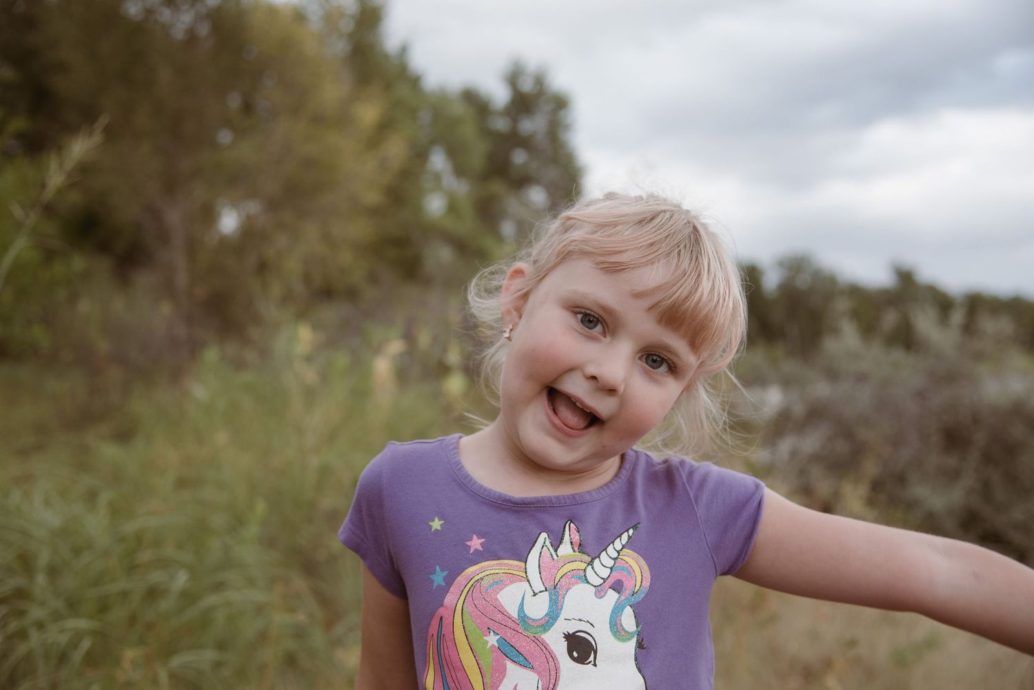 Happy young girl in a unicorn t-shirt smiling outdoors in a grassy field.