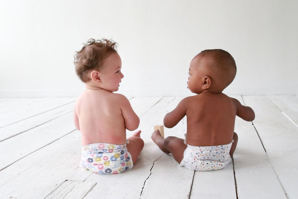 Two babies in diapers laughing together in a natural light studio