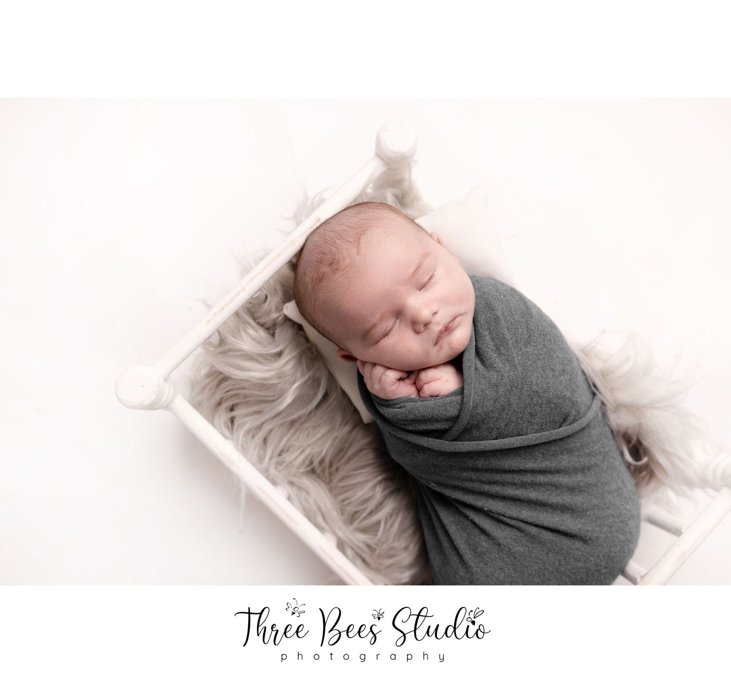 Sleeping newborn wrapped in gray swaddle on textured white blanket.