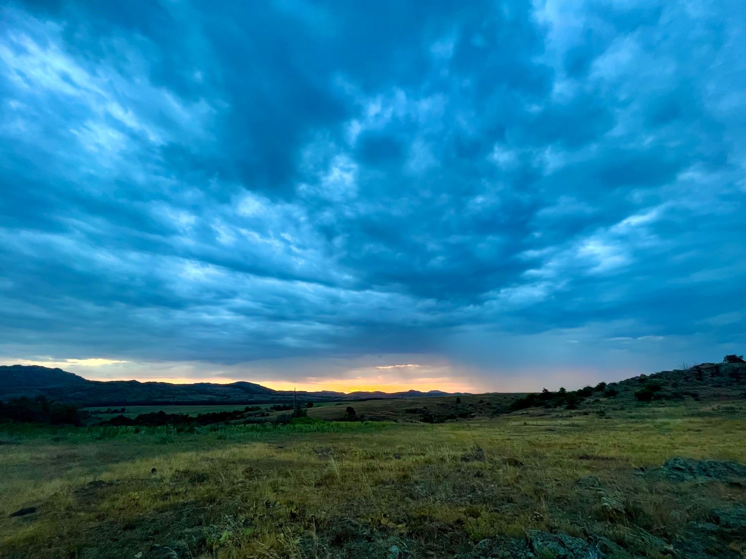 Wide-angle skyscape showing dramatic cloud formations over rolling hills.