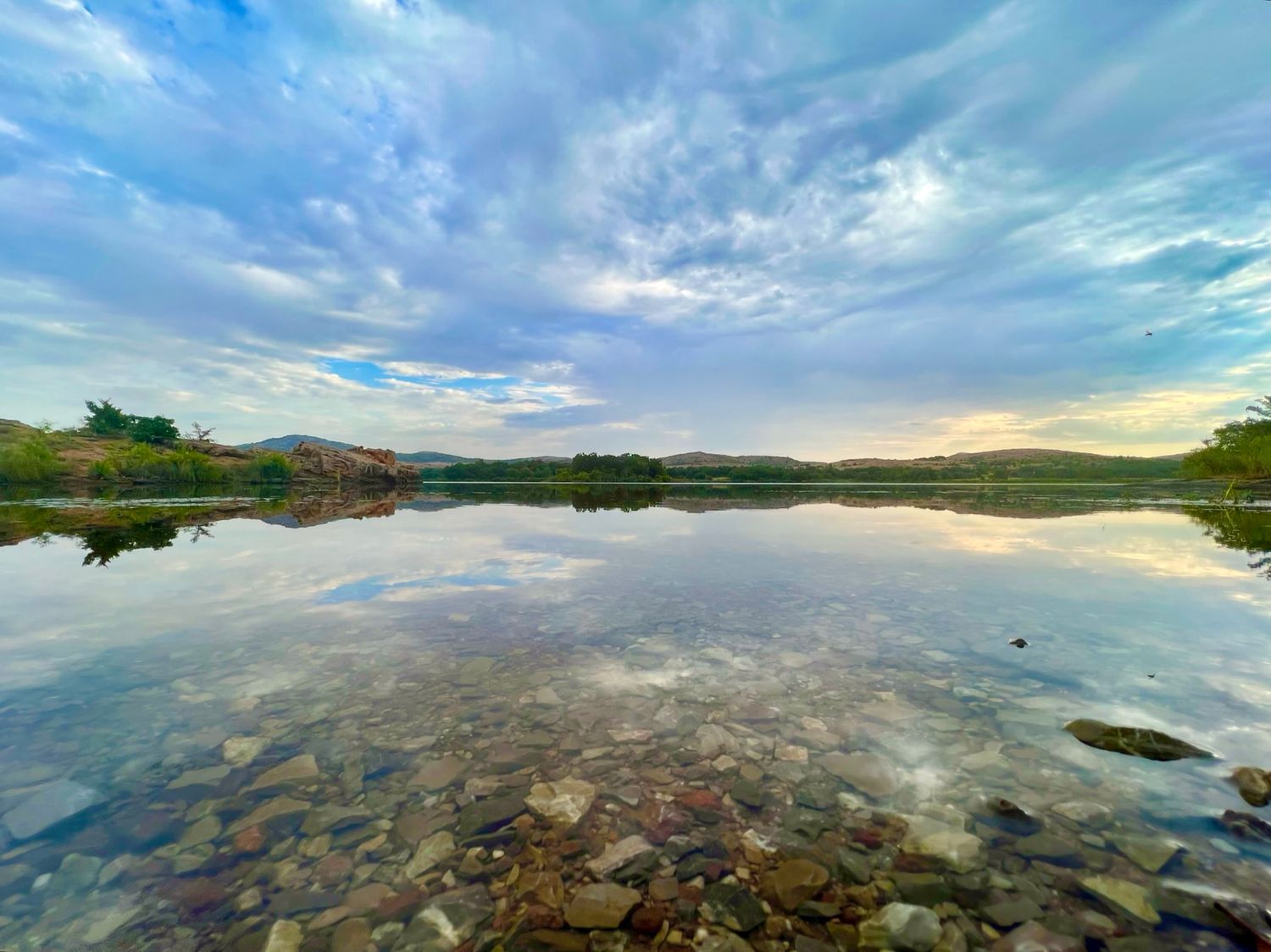 Panoramic landscape view of a serene lake reflecting dramatic clouds at sunset.