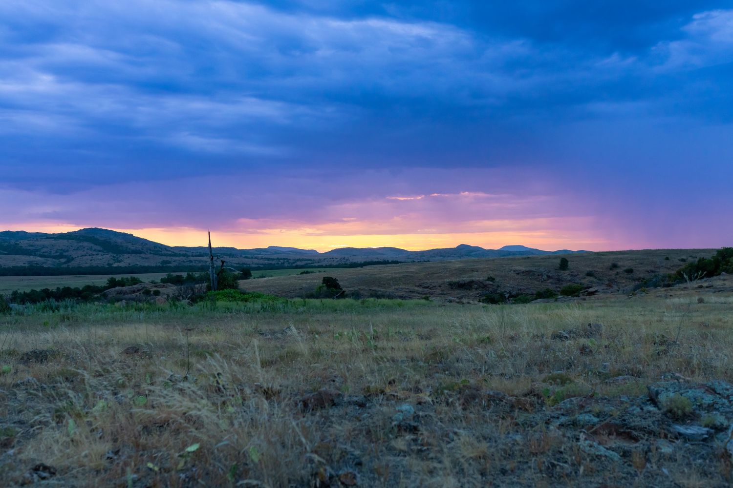 Panoramic sunset view over mountains with vibrant purple and orange sky.