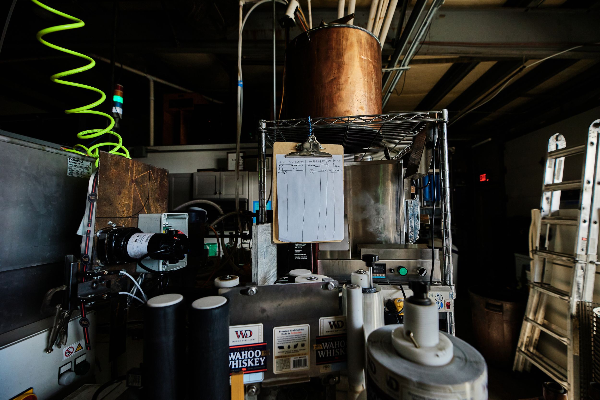 Industrial distillery equipment and storage tanks in a dimly lit warehouse setting.