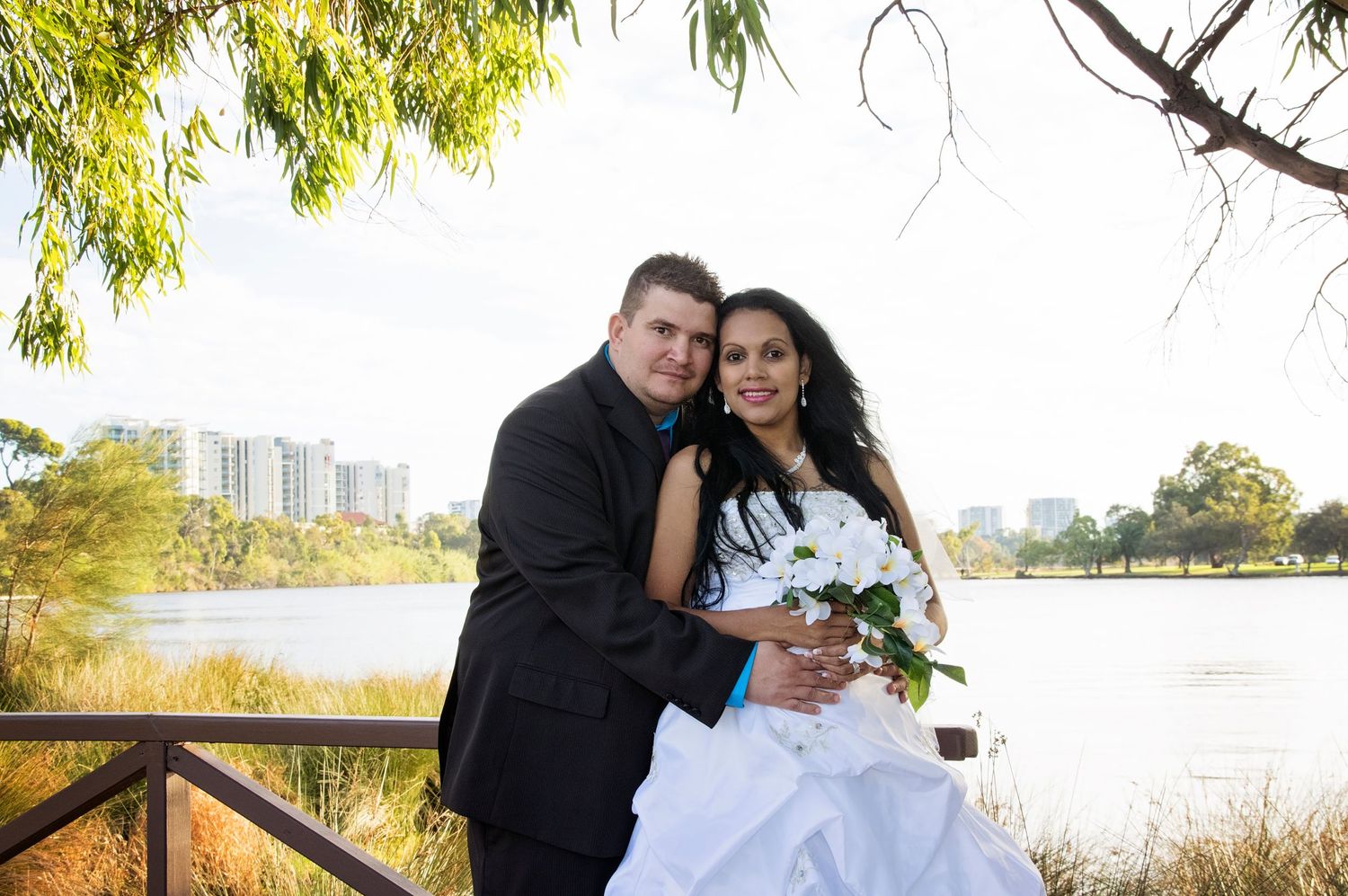 bride and groom smiling at camera on bridge