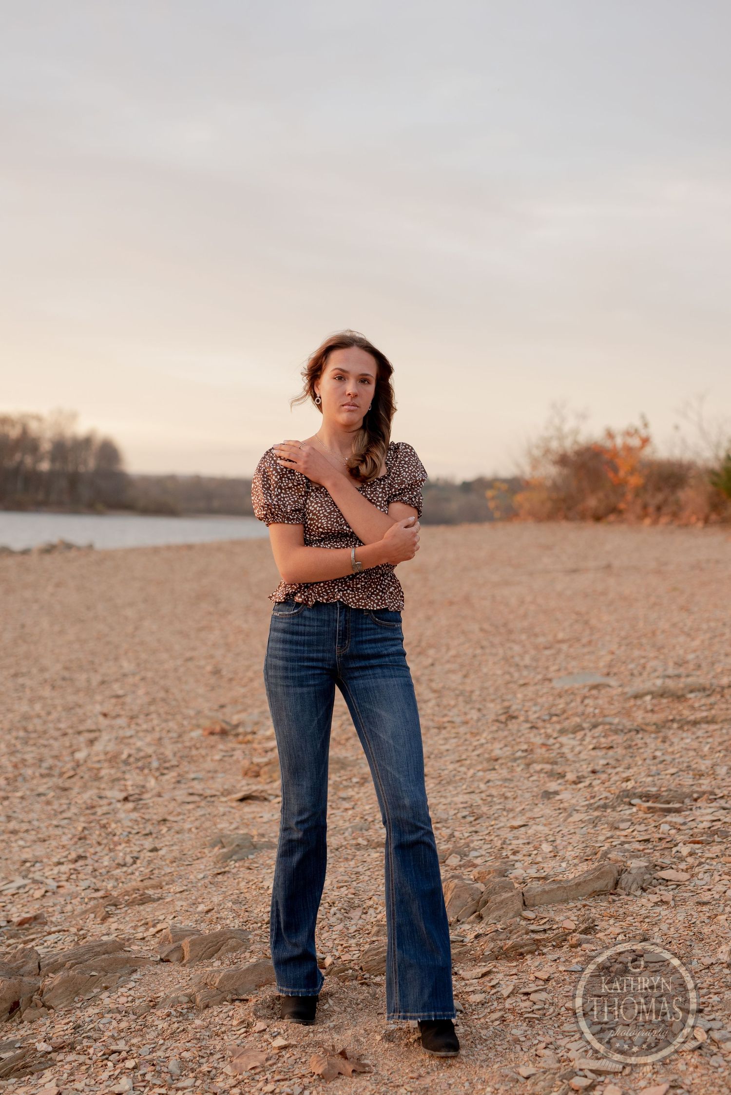 Portrait on sandy terrain by a lake with autumn trees in the background.