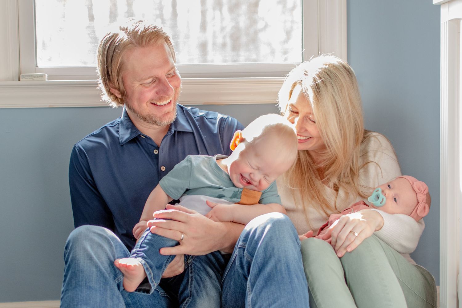 Family of four relaxing together on couch with twin babies in casual home setting.