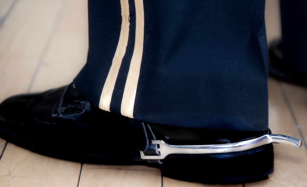 Close-up detail of military dress uniform pants with gold stripes and polished black shoes.