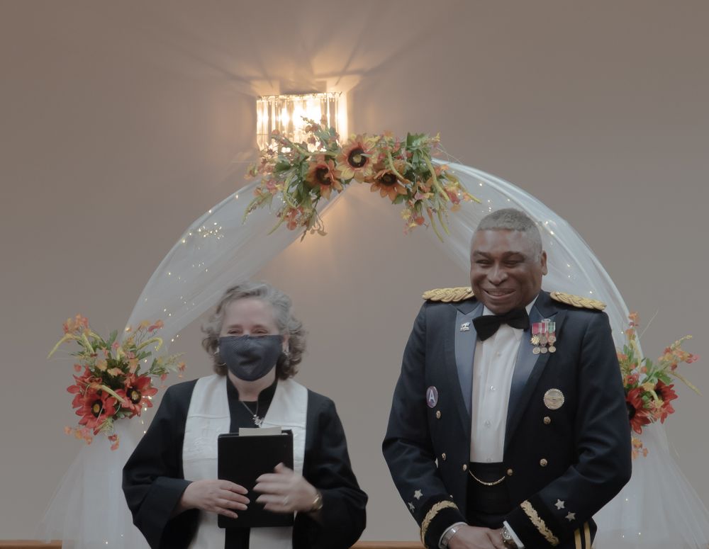 Wedding ceremony under decorated arch with floral arrangements and lighting.
