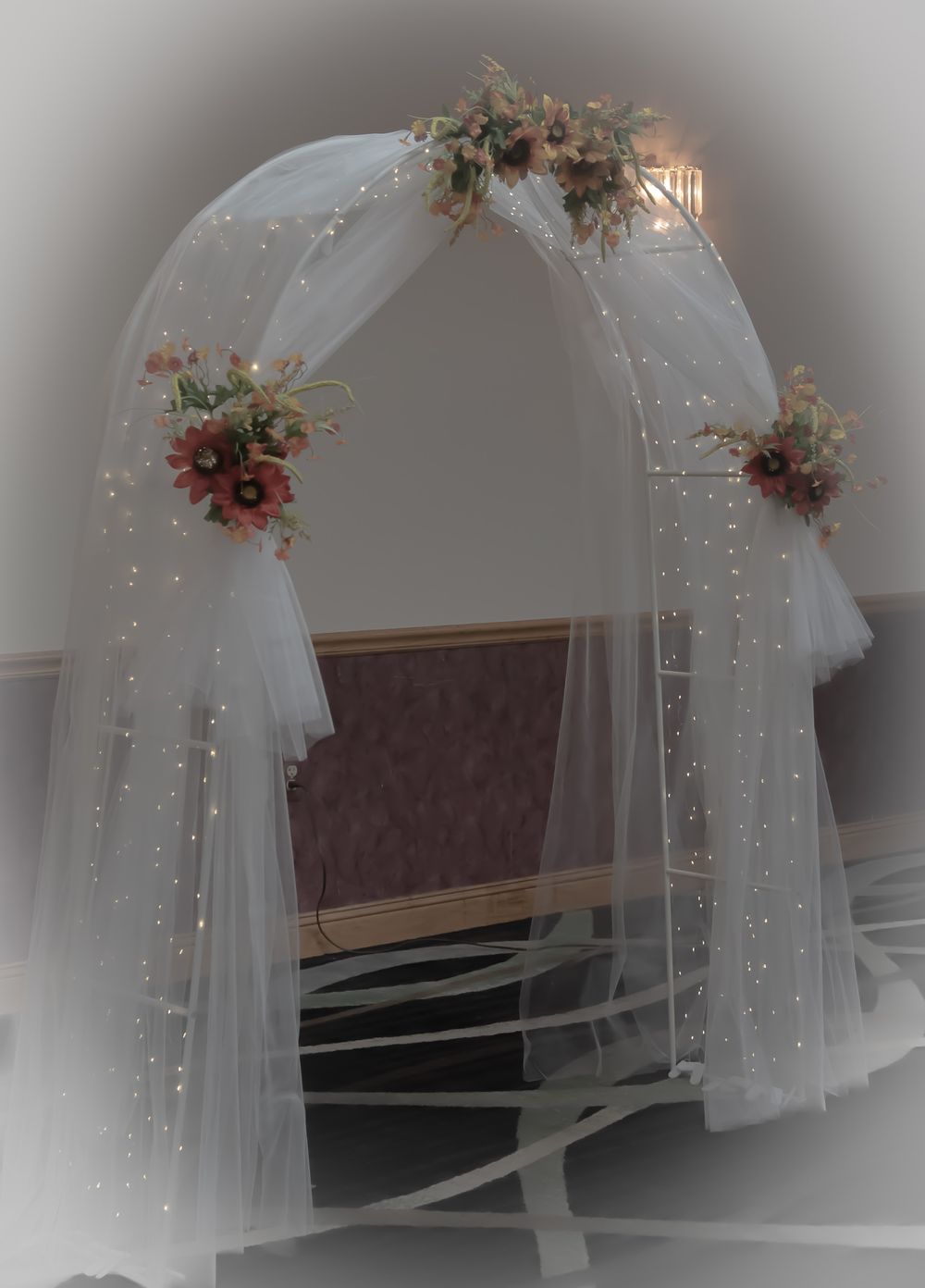 White wedding arch decorated with fairy lights, tulle and floral arrangements.