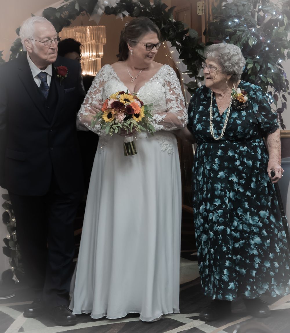 A wedding scene with a bride in a white lace dress holding a sunflower bouquet alongside guests in formal attire.
