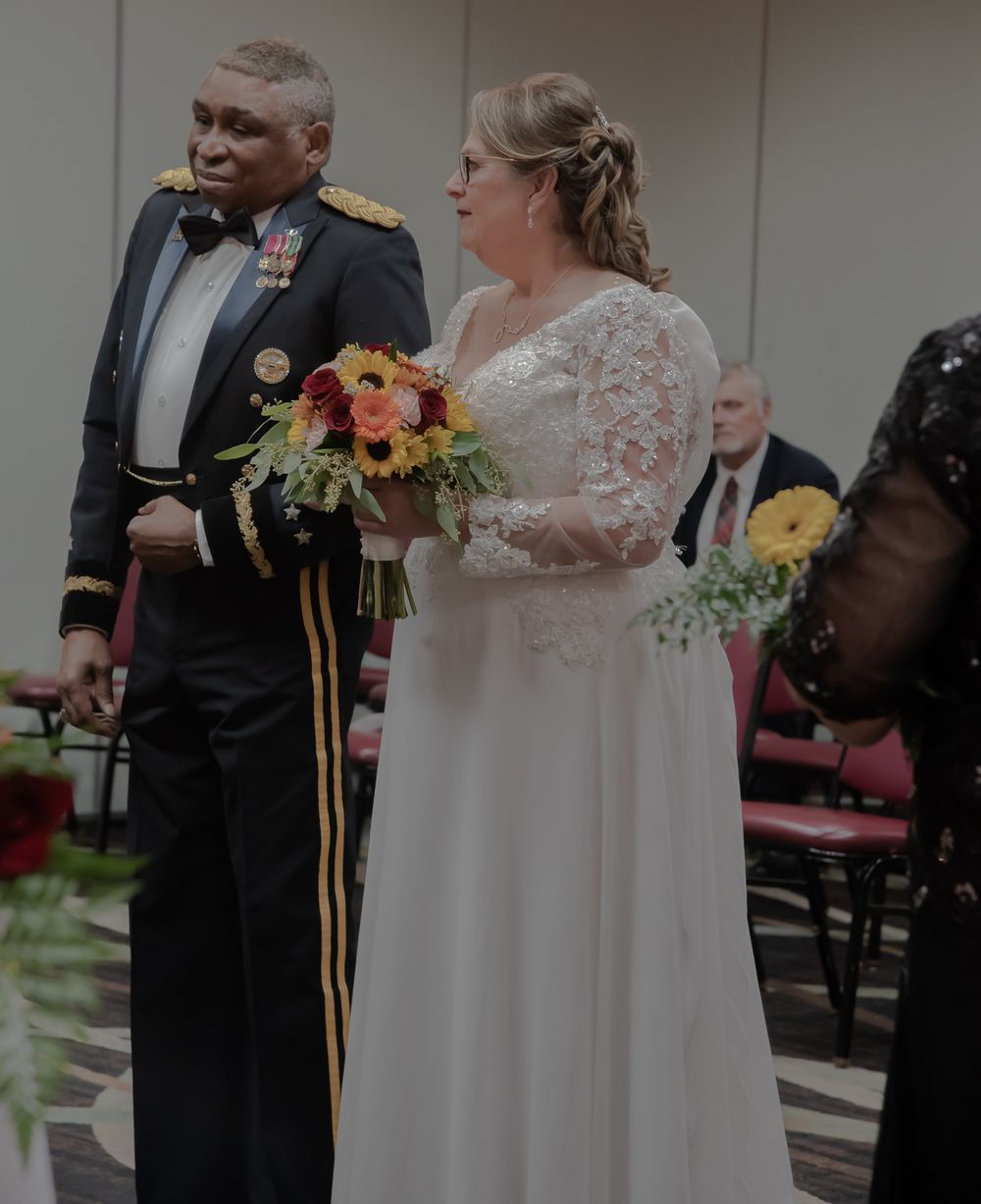 A military officer and bride stand together during their wedding ceremony with autumn-colored floral bouquets.