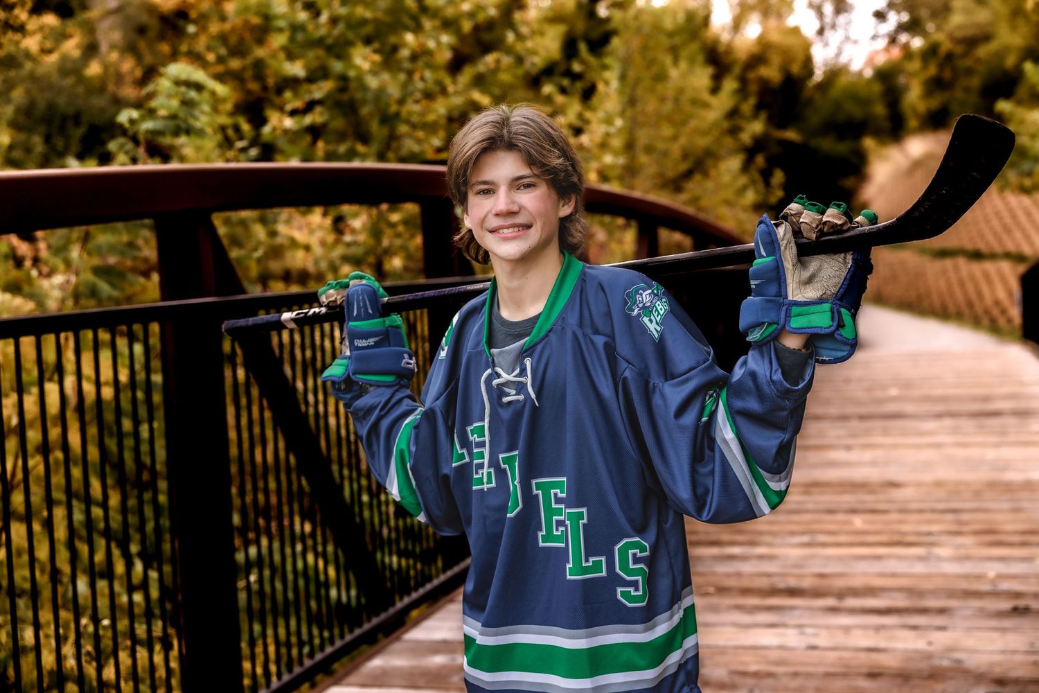 Person wearing hockey jersey posing with stick on wooden bridge during autumn.