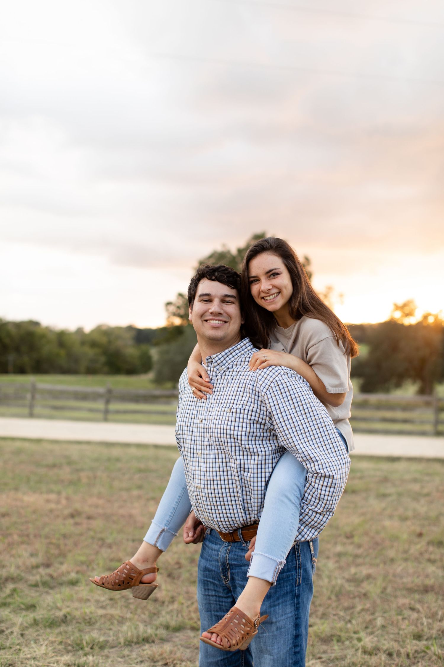 Couple shares a playful piggyback ride moment in a field at sunset.
