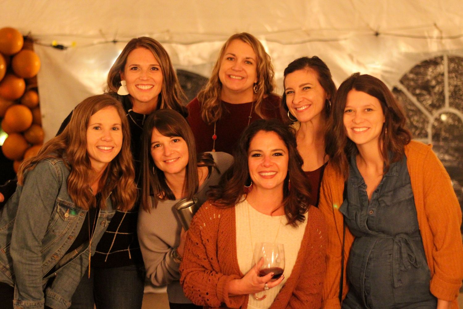 A group of friends smiling and celebrating together at an indoor party with rustic decor in warm lighting.