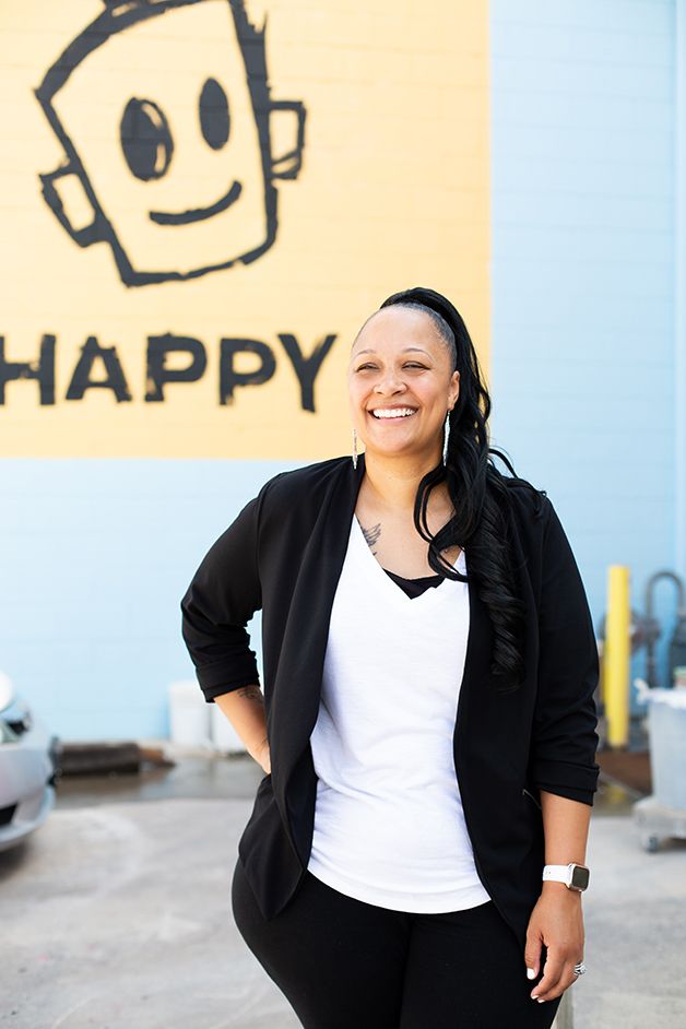 Woman in business attire smiling in front of the Happy mural in downtown Augusta, GA.