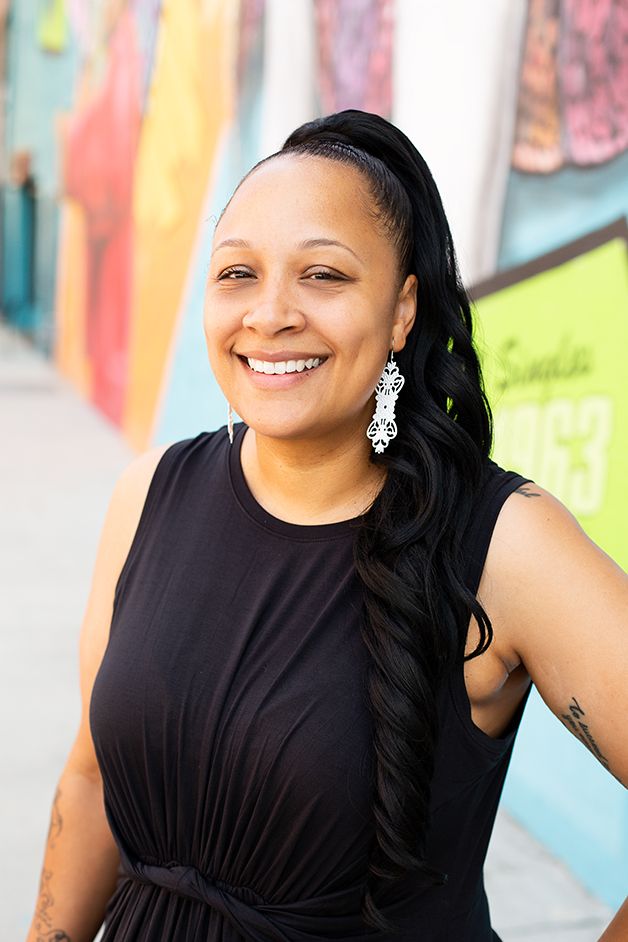 Woman with a black dress headshot with colorful downtown mural in background.