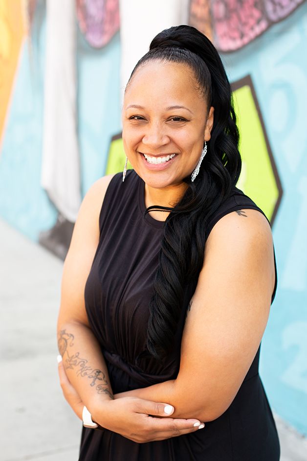 Woman in black dress smiling at the camera with mural in the background.
