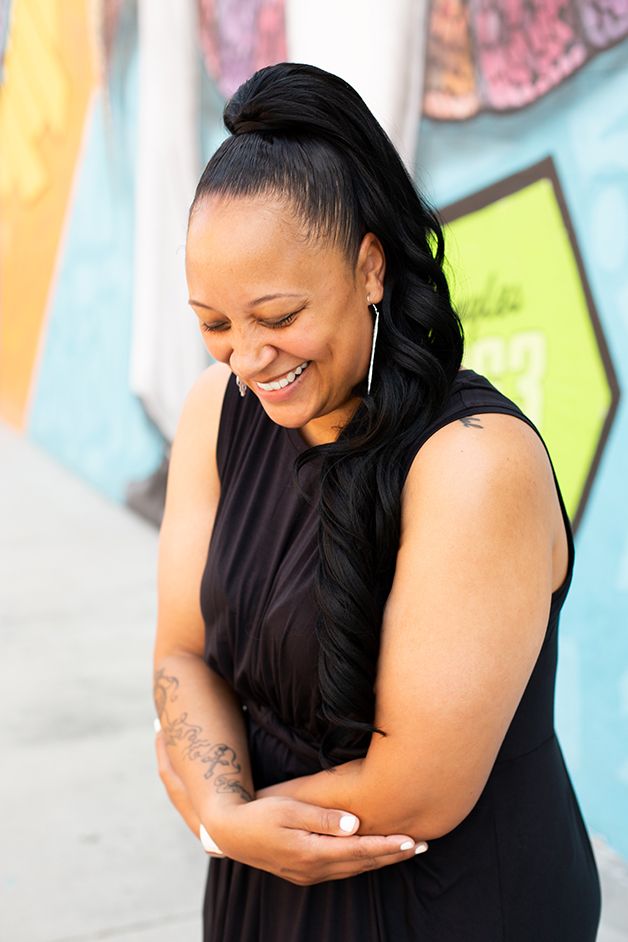 Woman in black dress laughing with a colorful mural behind her.