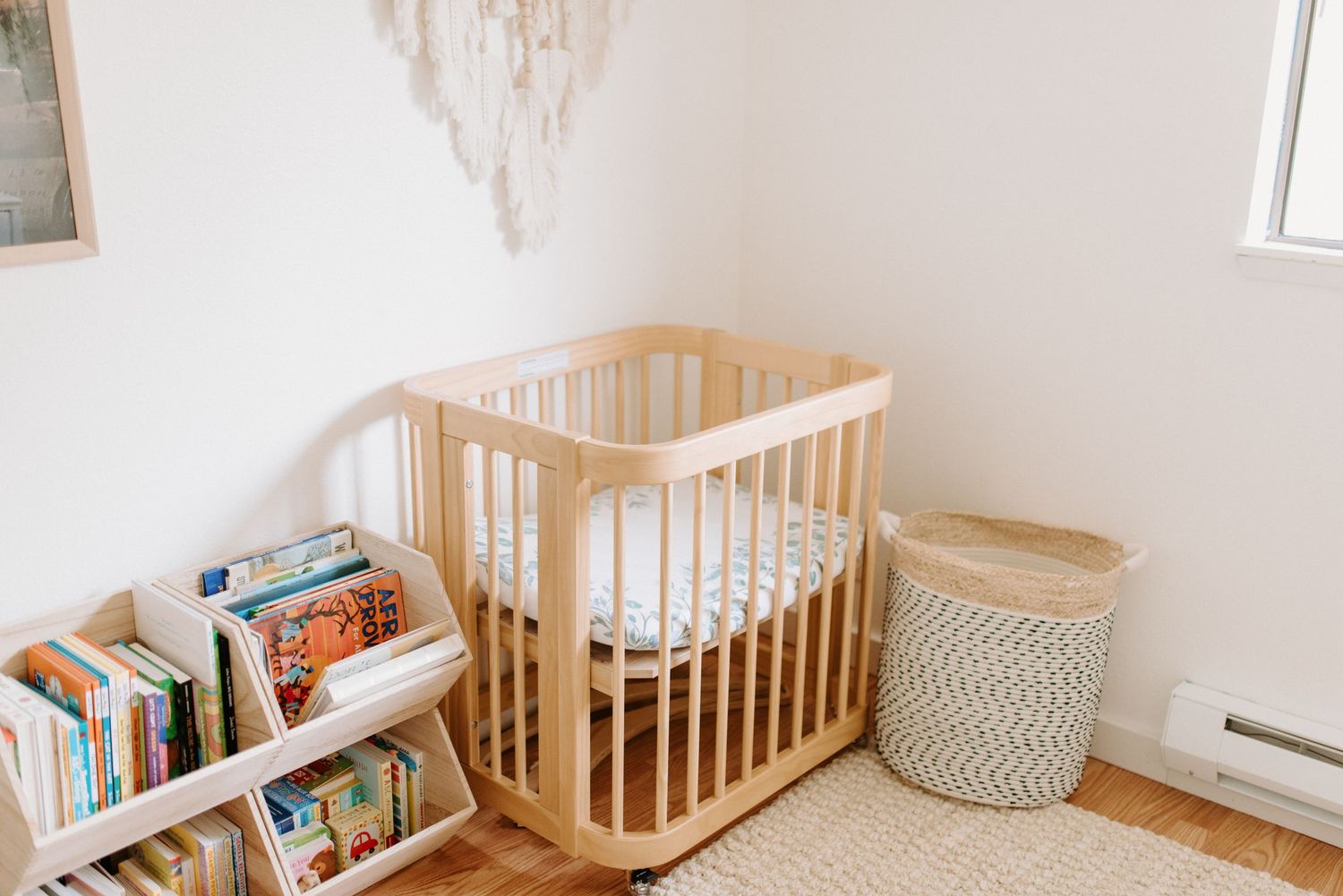 Light and airy nursery with natural wood crib, bookshelves, and white walls.