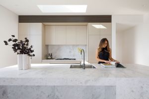 Modern minimalist kitchen featuring sleek white cabinets and luxurious marble waterfall countertop with black floral arrangement.